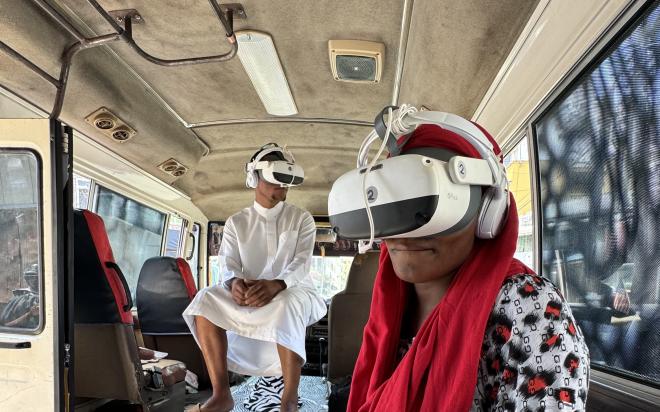 2 Besucher*innen sitzen mit VR Brillen im Daladala (Bus).