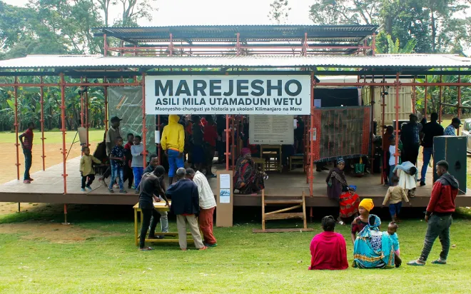 Foto der Marejesho Ausstellung, ein offener Bau auf einer Wiese mit Besucher:innen