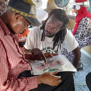 Artistic director Isack Abeneko shows a map to a visitor of Ultimate Safari