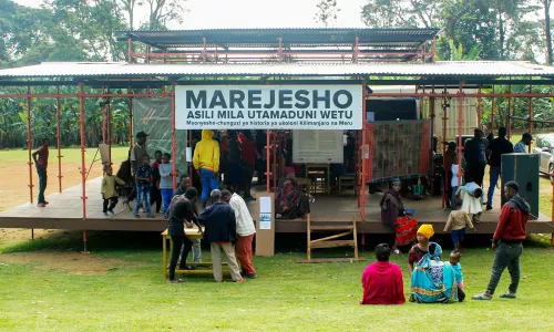 Foto der Marejesho Ausstellung, ein offener Bau auf einer Wiese mit Besucher:innen