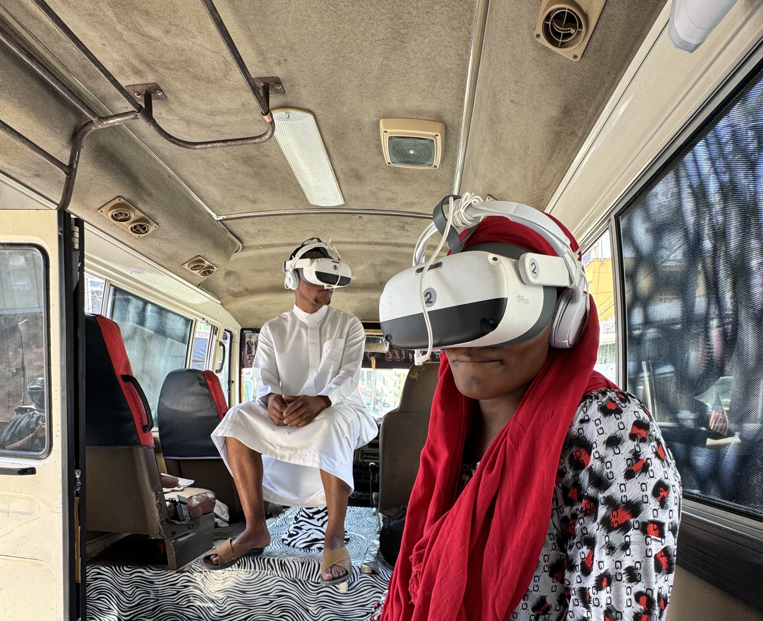 2 Besucher*innen sitzen mit VR Brillen im Daladala (Bus).